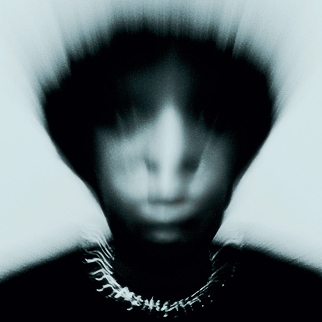 Gallant's Zinc album cover features a blurred portrait of him with an indistinct face, wearing a necklace, set against a dark, monochromatic background, creating a mysterious and eerie atmosphere.