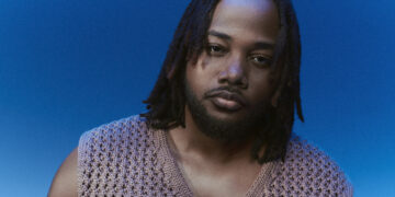 A photo of singer, songwriter and producer Leon Thomas against a blue backdrop.