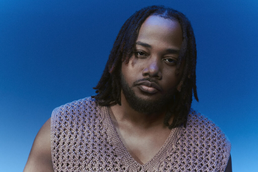 A photo of singer, songwriter and producer Leon Thomas against a blue backdrop.