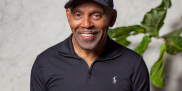 A photo of Frankie Beverly standing in front of a wall with a green plant